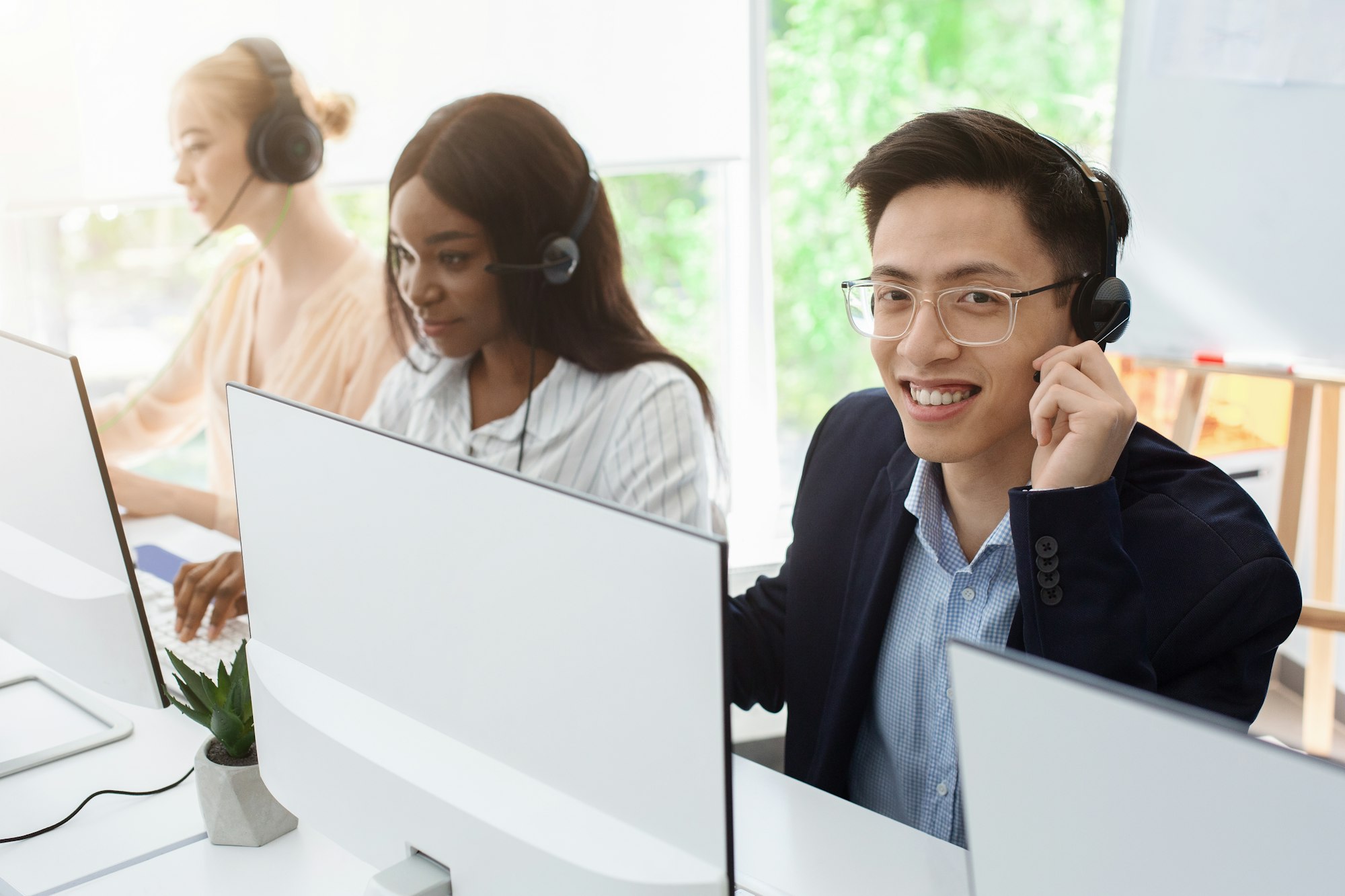 Customer support phone operators in headsets behind computer monitors at call center, empty space